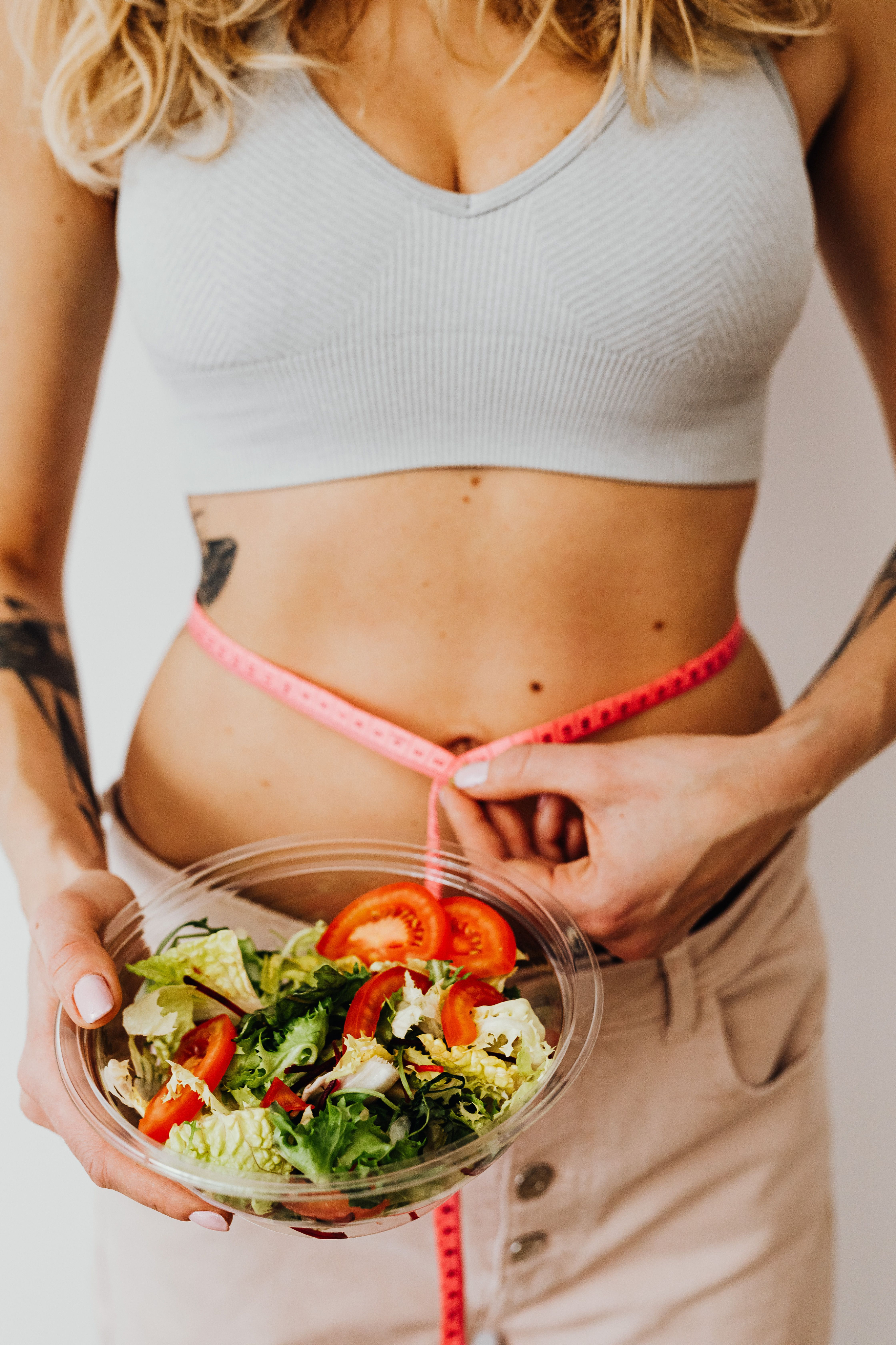 Woman holding a salad bowl and measuring her waist with a pink tape